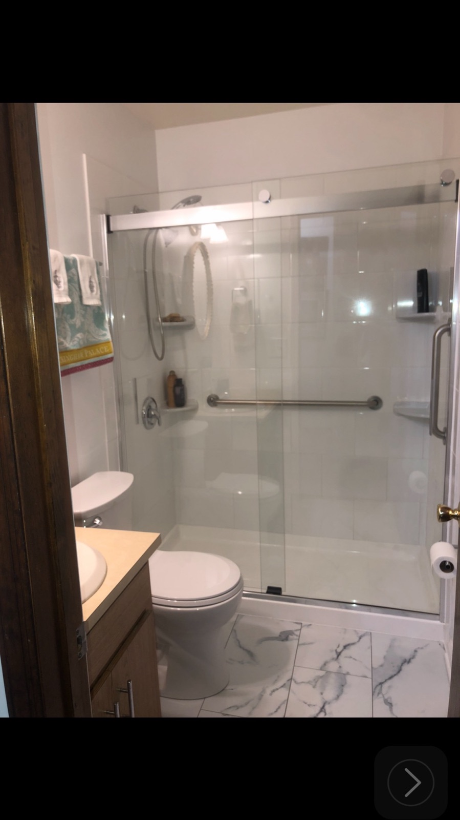 Bathroom remodel with glass sliding shower doors, marble-look tile floor, and grab bars