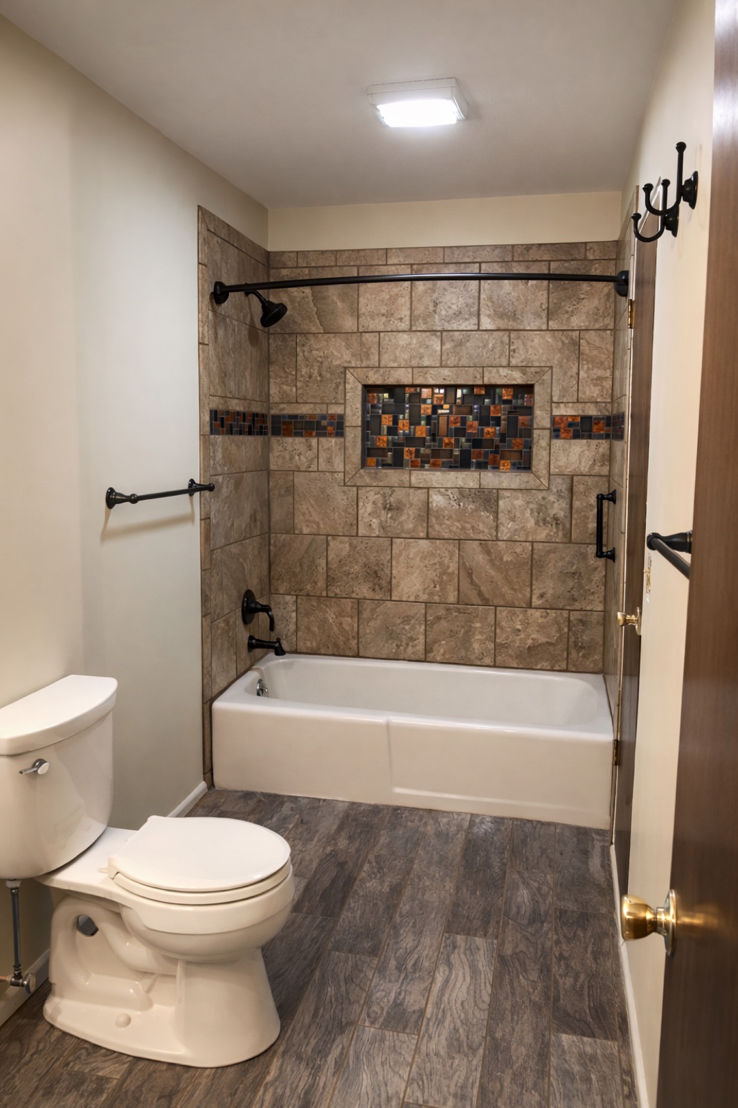 Full bathroom remodel with travertine stone tile shower surround, mosaic accent band, and wood-look floor